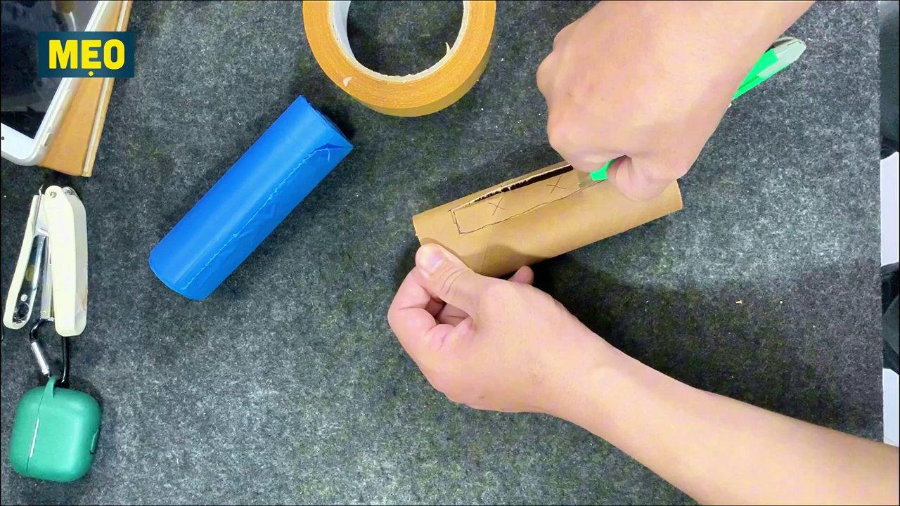 Một cuộn túi rác được đặt dưới đáy thùng, đầu túi được luồn lên qua lỗ đã cắt trên thân thùng.